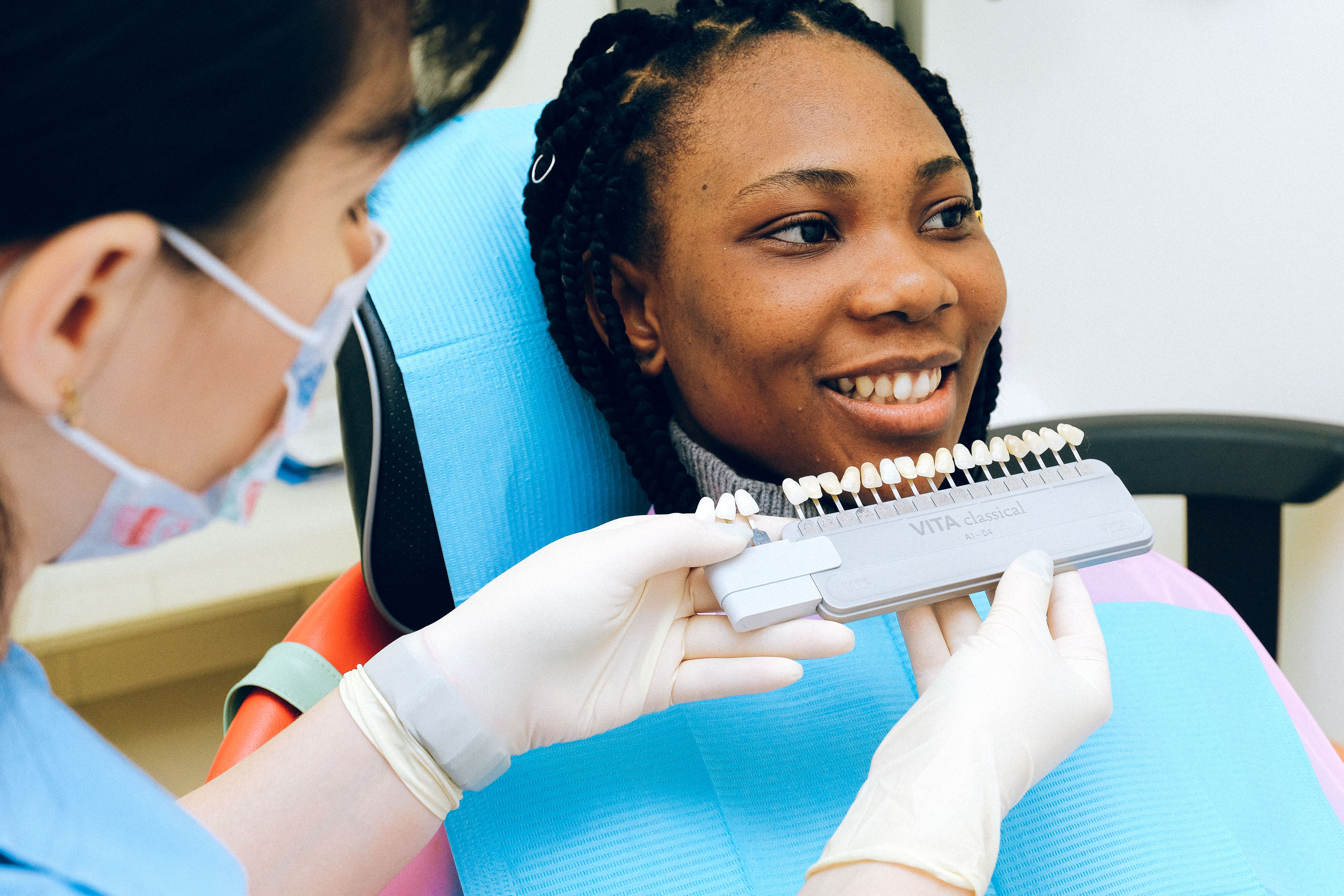 A dentist matching a shade guide against a smiling patient's teeth
